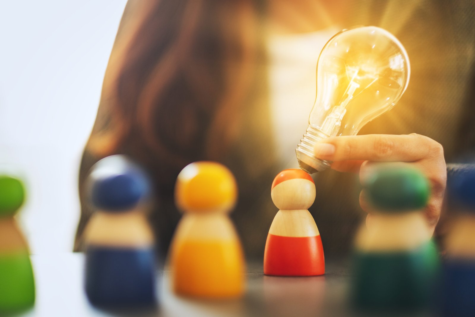 Closeup image of a woman holding and putting a light bulb over one of a different colors wooden people toy for business concept